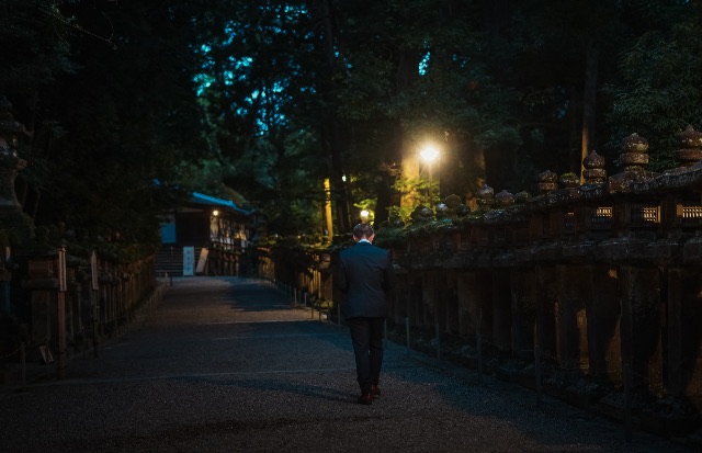 Back view of a well-dressed man walking down a quiet illuminated stone path at night in Japan